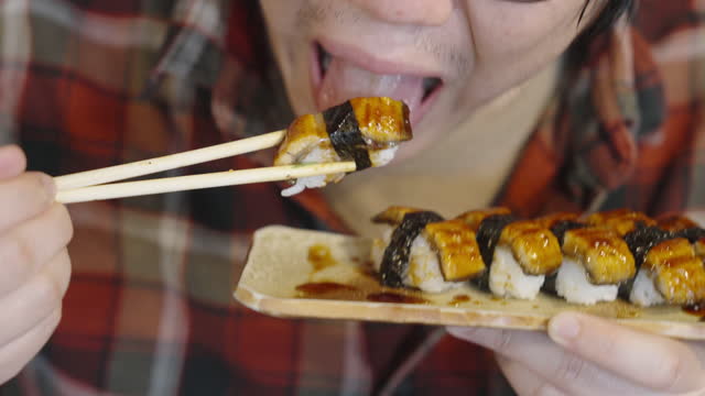 Hungry man holding chopsticks eating unagi sushi with teriyaki sauce