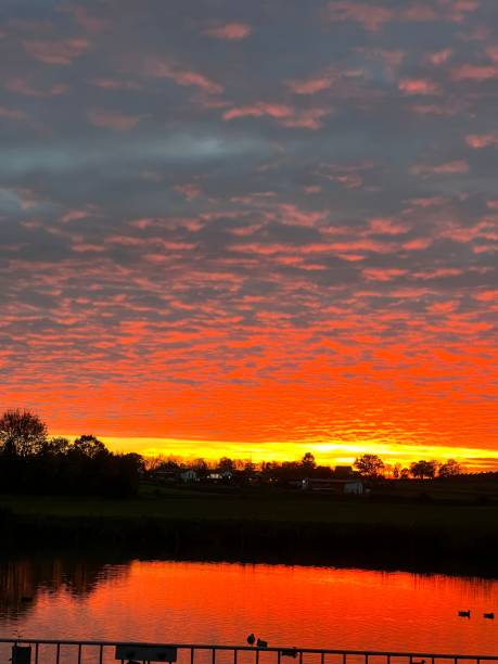 istock Mesmerizing scene of orange cloudy sky over reflecting lakw wih trees 1452545604