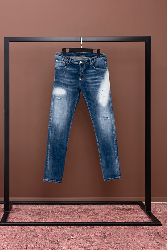 Blue jeans hanging on a hanger. Clothes hanging in front of brown background.