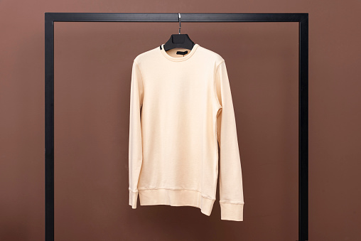 Yellow sweatshirt hanging on a hanger. Clothes hanging in front of brown background.