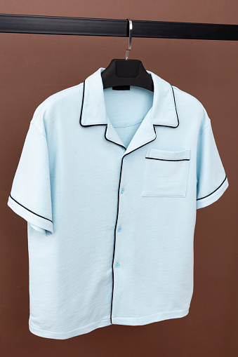 Blue patterned shirt hanging on a hanger. Clothes hanging in front of brown background.