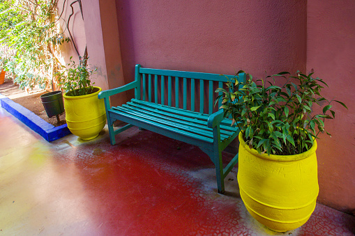 Plants in pots and a green bench on a crimson wall in the famous Majorelle Garden in Marrakesh, pink wall and terracotta color on the floor