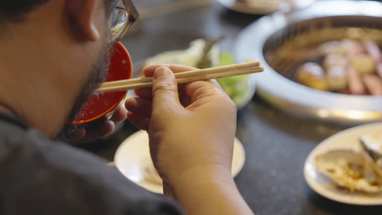 A large build person eating rice from a nearly empty bowl with chopsticks in a Japanese restaurant