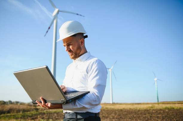 inżynier stojący i hodujący laptopa z turbiną wiatrową. - engineer environment factory orange zdjęcia i obrazy z banku zdjęć