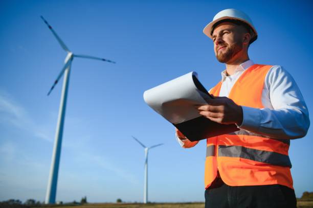 istock Engineer is checking energy production on wind turbine. Worker in windmills park in helmet. 1452556178