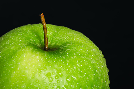 Green apple in drops of water on a black background isolated, macro shot.