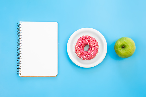 Blank notepad, donut and apple on blue background, flat lay, copy space.