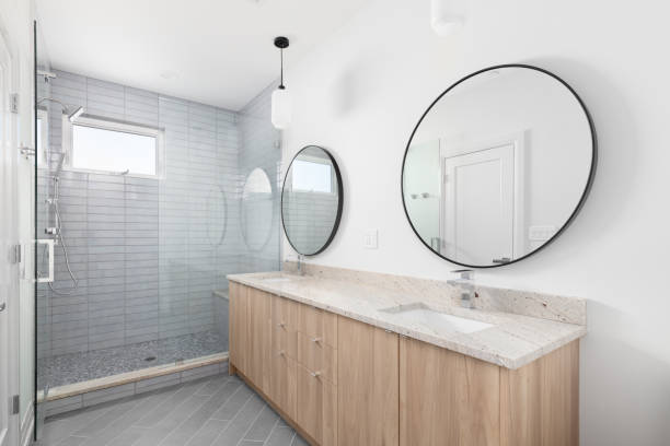 istock A bathroom with a wood cabinet, circular mirrors, and a tiled shower. 1452561571