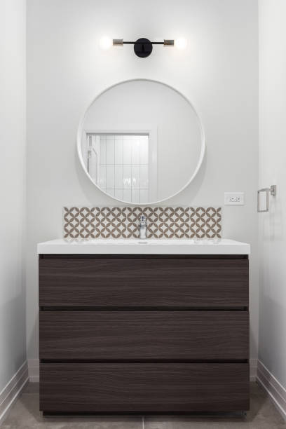 istock A bathroom with a wood cabinet, circular mirror, and tile backsplash. 1452562164