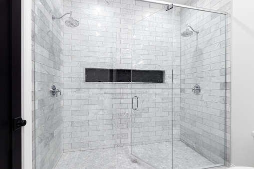 A large, luxury double shower with marble subway tile walls, marble hexagon floor, and black hexagon tiled shelf.
