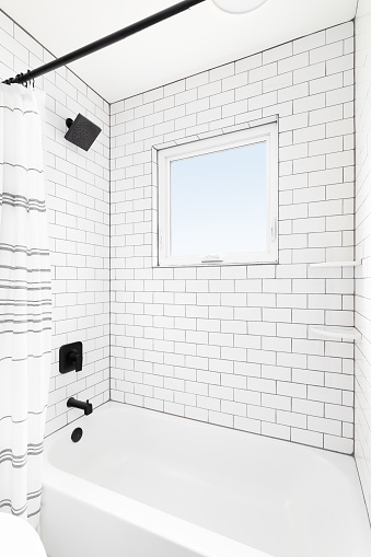 A shower with white subway tiles, window, and a black shower head.