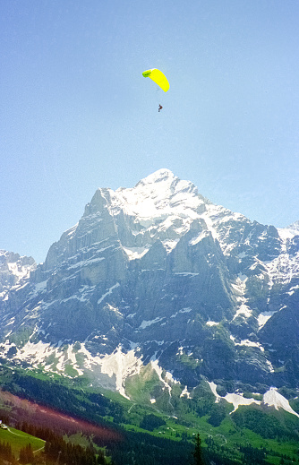 Grindelwald, Switzerland - 1982: A vintage 1980's Nikon negative film scan of the snow covered Swiss Alps mountains surrounding the small town of Grindelwald, Switzerland with a person parachuting down from the sky.