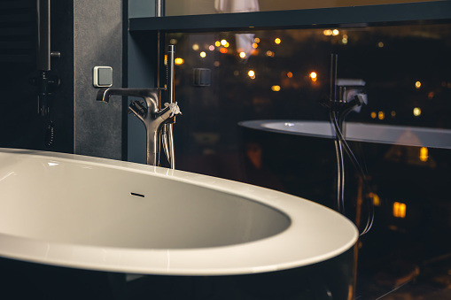 The interior of a modern bathroom with a window overlooking the night city, copy space.