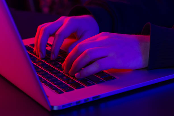 A man uses a laptop, close-up, male hands in neon lighting. stock photo