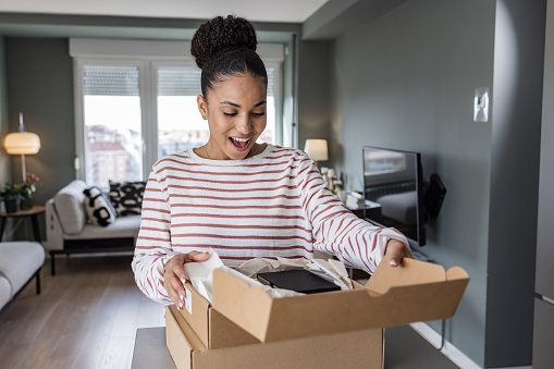 African-American woman unpacking parcel that she ordered from an online store. Online shopping and shipping service concept.