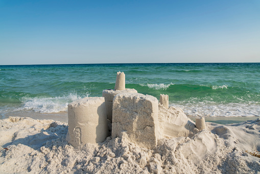Destroyed sand castle against the ocean waves at the beach in Destin, Florida. Close-up of a sand castle near the waves of the ocean under the blue sky.