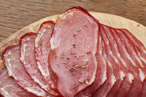 A top view of a dry ham slices with a herb seasoning on a wooden cutting board, an image with a copy space