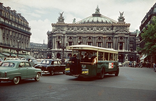 Paris, Il de France, France, 1959. Street scene at Place de l'Opéra. In the background the Opéra Garnier. Also: road traffic, Parisians, tourists and public transport.