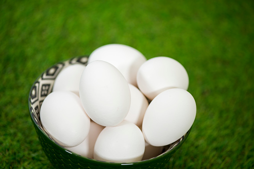 Closeup of farm fresh white chicken eggs sitting in a bowl against a green grass background.