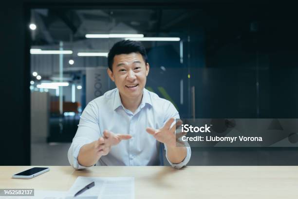 An Asian Man Sitting In The Office And Talking To The Camera Online Meetings Business Training Stock Photo - Download Image Now