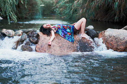 portrait mid adult latina woman lying down with eyes closed resting on a rock in the river rural area disconnection from the real world
