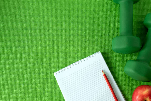 istock Two dumbbells with blank notebook, and red apple on green workout mat background, top view, copy space 1452586051