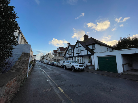 Jersey Island is one of the channel islands of the United Kingdom. This is a street in the St. Helier district, between residential terraces, with cars parking along the street. There is a blue sky with some clouds.