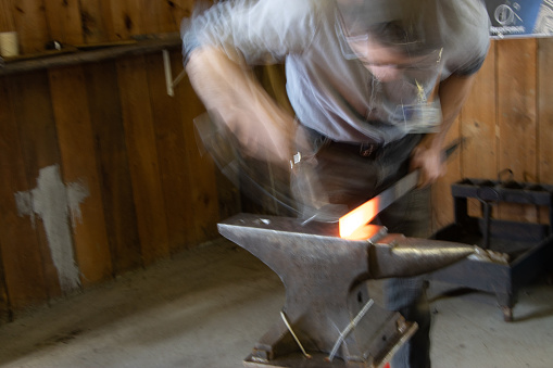 Close-up of unrecognizable person blacksmith bending wrought iron while hitting metal with hammer on anvil