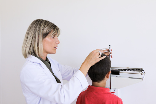 Argentinean nutritionist woman mesuring height and weight of a 8 years-old boy at proffesional balance in the medical office during a medical control - Buenos Aires - Argentina