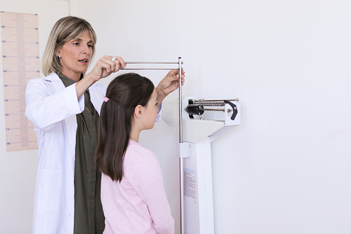 Argentinean nutritionist woman mesuring height and weight of a 9 years-old boy at a balance in the medical office during a medical control- Buenos Aires - Argentina