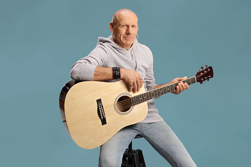 Musician with an acoustic guitar seated on a chair isolated on blue background