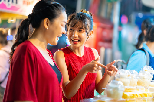 Happy Asian family on summer holiday travel vacation. Adult mother and daughter enjoy and fun outdoor city lifestyle shopping and eating street food together at Bangkok Chinatown street night market.