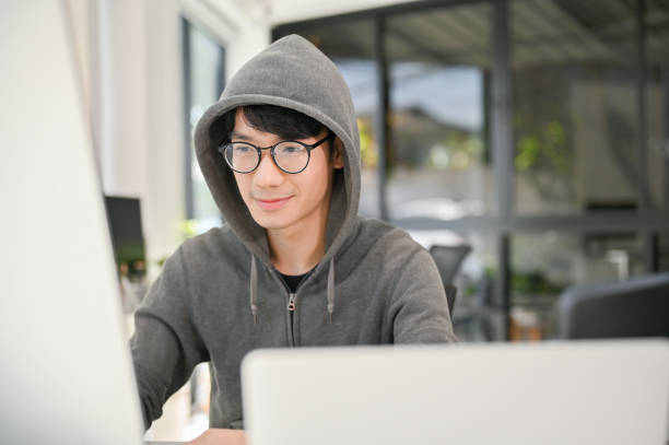 Smart and nerd young Asian male website developer or programmer working in the office. Smart and nerd young Asian male website developer or programmer wearing eyeglasses and hoodie sweater focusing on his task on computer, working in the office. nerd sweater stock pictures, royalty-free photos & images