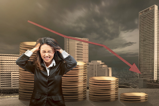 Asian businesswomen are frustrated with a decreased coin graph with a cityscape background