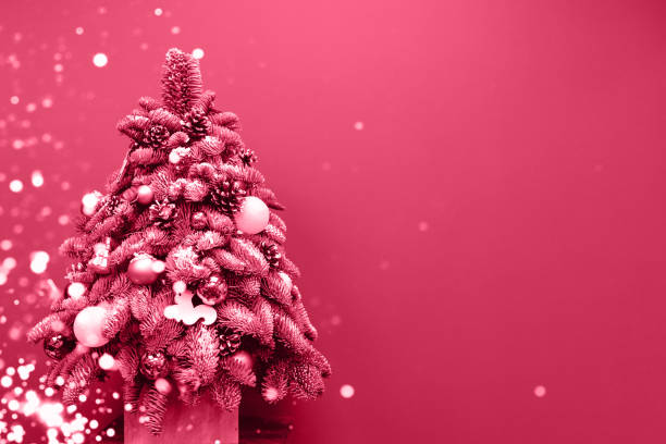 Beautiful Christmas tree decorated in lights on a magenta background. Trendy color 2023.
