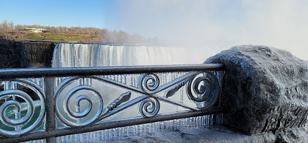 A scenic shot of an iced fence in front of the Niagara Falls in Canada in winter
