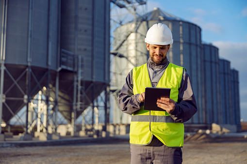 A supplies worker uses a tablet in front of the silos.