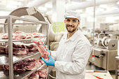 A meat factory worker is holding piece of raw meat and smiling at the camera.