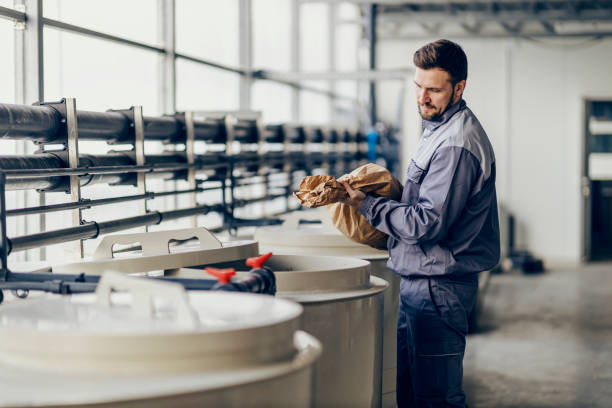 A worker is putting grains into containers while standing in barn storage. An industry worker is putting sack of grains into containers at barn storage. plant fertilizer stock pictures, royalty-free photos & images