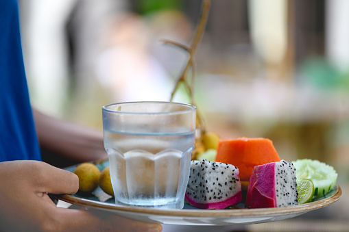 A waiter brings a plate of fresh tropical fruits and vegetables and a full glass of cold water