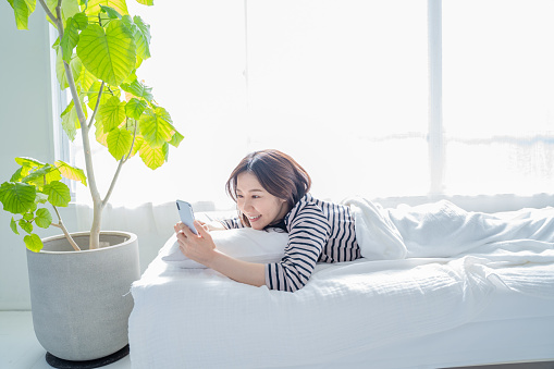 Smiling woman looking at smartphone screen in bed.