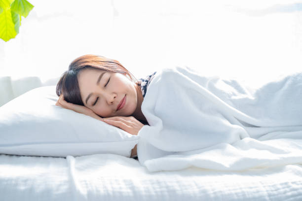 A woman sleeping on a bed in a bright simple room.