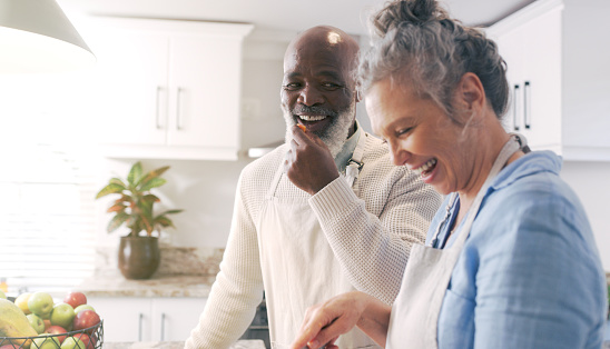 Love, senior couple and eating in kitchen while cooking a gourmet meal. Romance, food and elderly, retired and interracial couple, man and woman talking, having fun or enjoying quality time together.