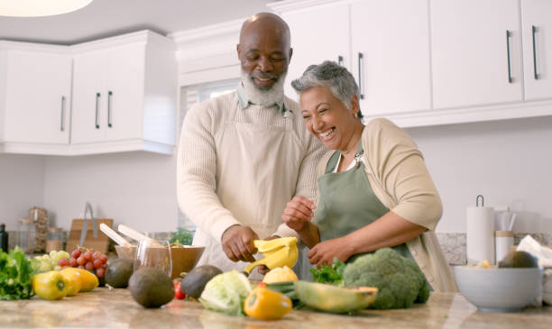 cocina, cocina y senior con una pareja negra riendo mientras preparan una comida juntos en su casa. comida, salud y diversión con un hombre y una mujer maduros divirtiéndose o vinculándose en una casa de retiro - cooking senior adult healthy lifestyle couple fotografías e imágenes de stock