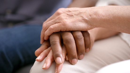 Hands, support and care with a couple in their home together for trust, love or console together. Holding hands, cancer and compassion with a man and woman in unity or solidarity during grief