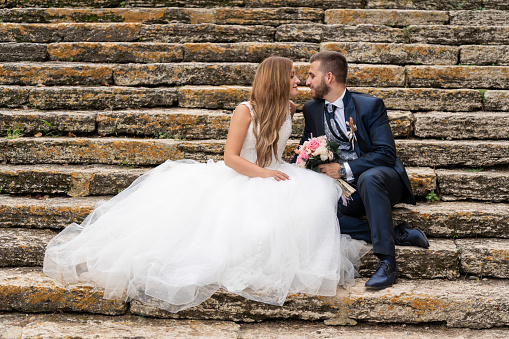 Portrait of newly married couple kissing and looking at each other on some stone stairs in the background