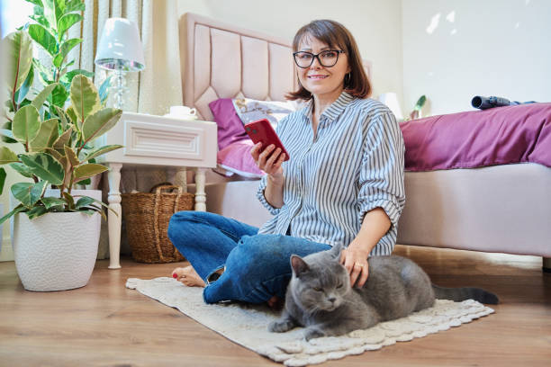 istock Female sitting on floor using smartphone, pet cat lying near owner 1452653316