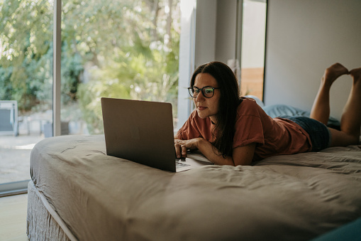 Woman lying on bed and using laptop at home in the morning