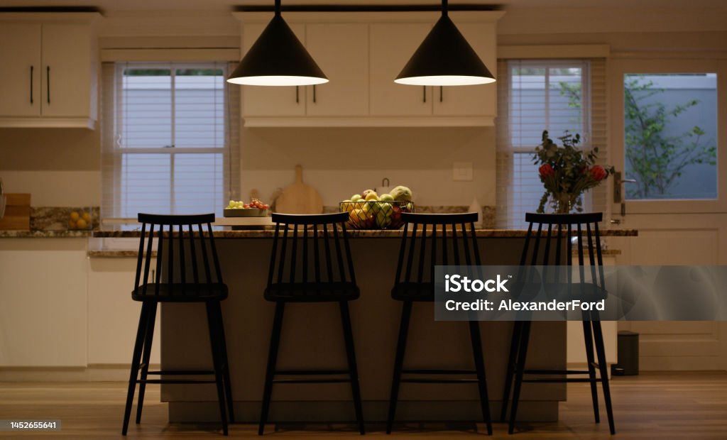 House, home and empty kitchen room for breakfast meal, lunch food or dinner social gathering at night or late evening. Chairs, furniture and counter top table and fruits basket, bar stool or comfort Kitchen Stock Photo