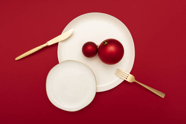 istock Elegant table setting with two plates, gold knife and fork and bright red christmas baubles on red background. Bold New Year concept. 1452656855